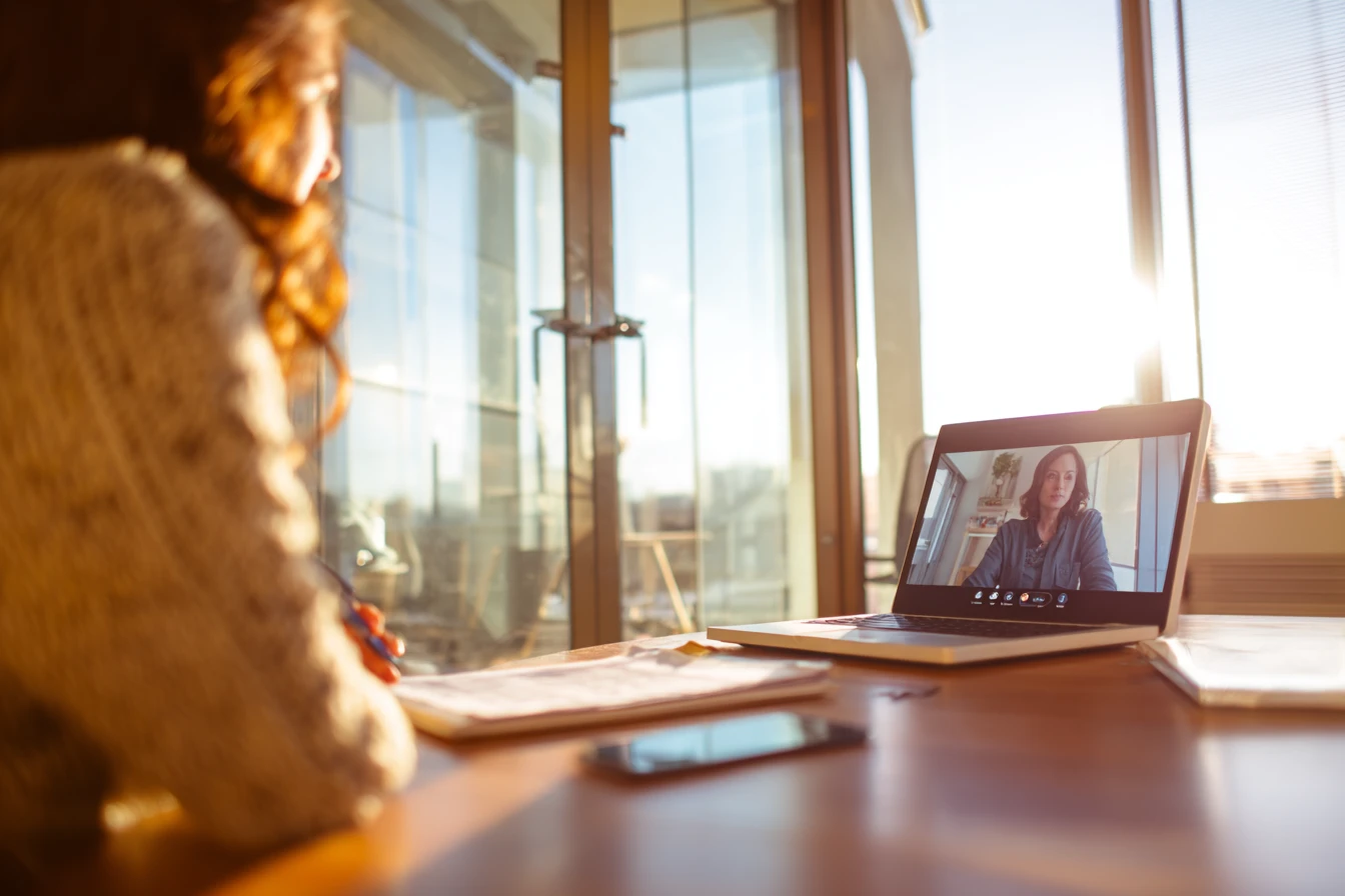 Practice manager on a video call with a vendor rep while reviewing a printed checklist, notes and laptop screen blurred