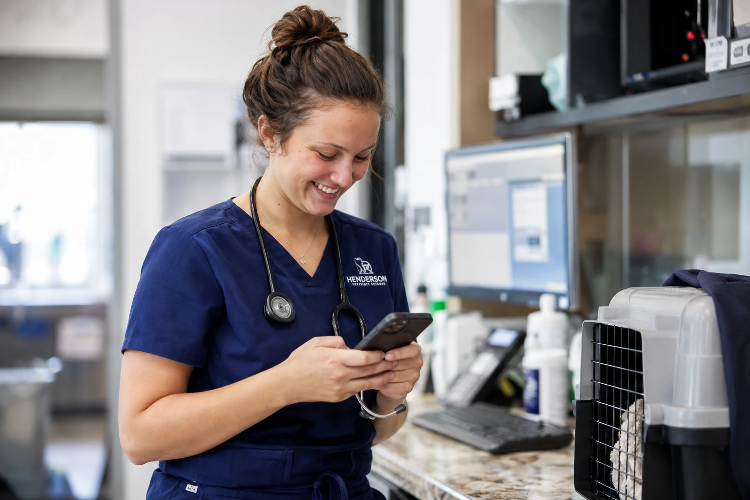 Veterinary technician sending a text message to a pet owner from a smartphone at the clinic workstation